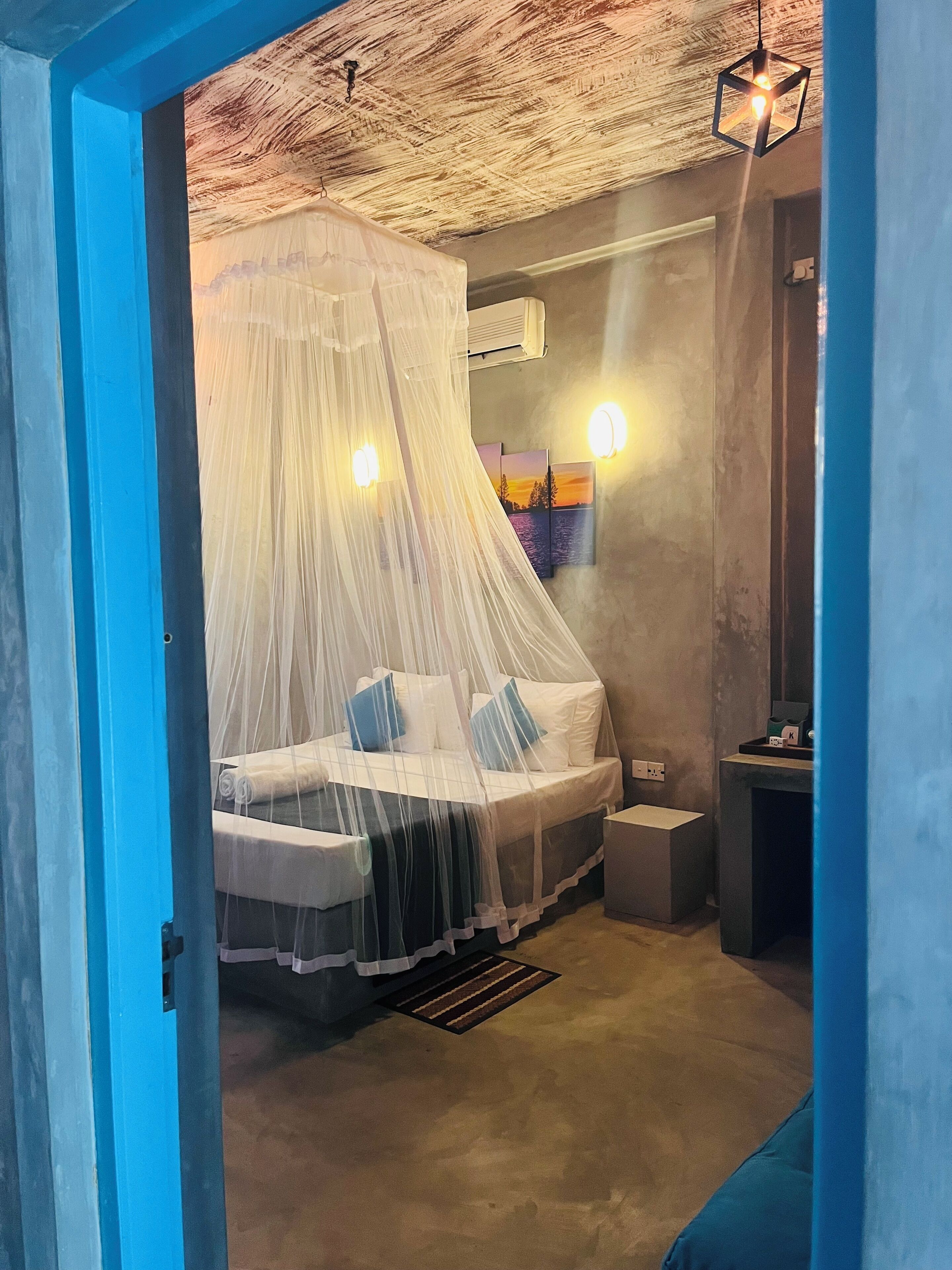 A bedroom with a bed under a canopy, a bedside table, a nightstand, and a wall-mounted air conditioning unit.