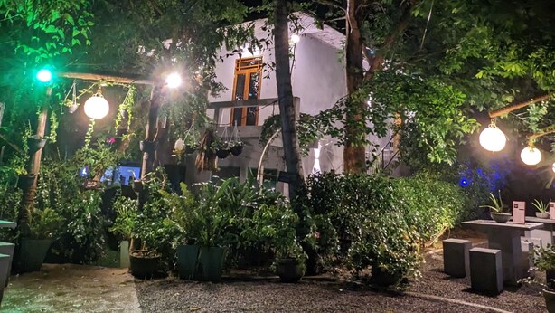 An outdoor garden area with a pathway, potted plants, and a building with a door and windows in the background. - Soul Villas (Tangalle)