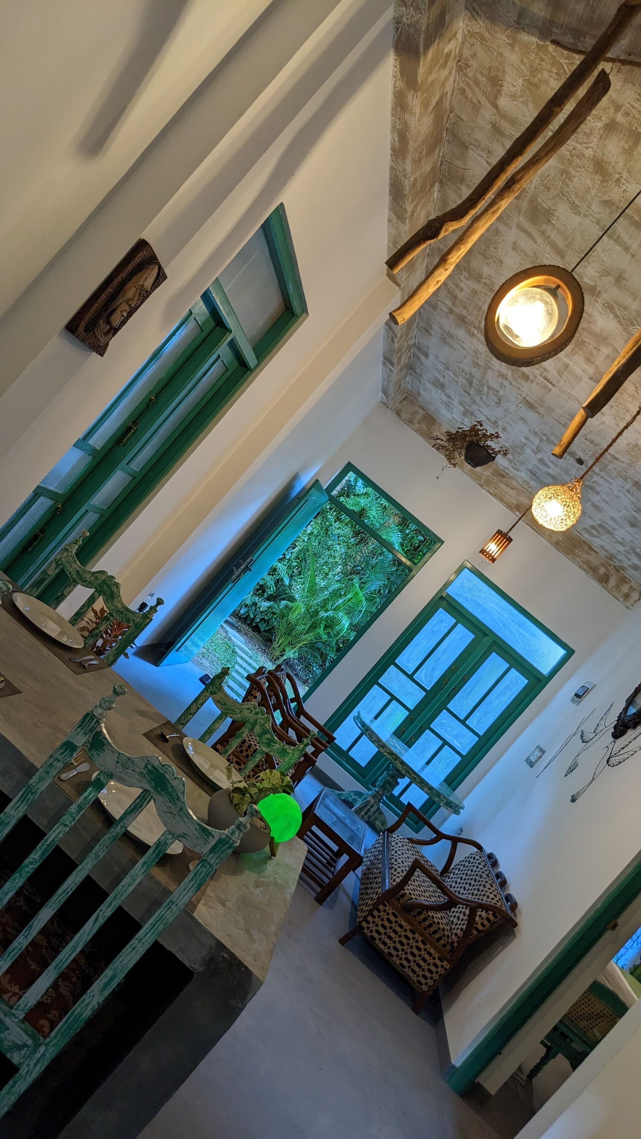 A spacious interior with a high ceiling, a staircase, and a view of a lush garden through a large window.