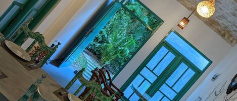 A spacious interior with a high ceiling, a staircase, and a view of a lush garden through a large window.