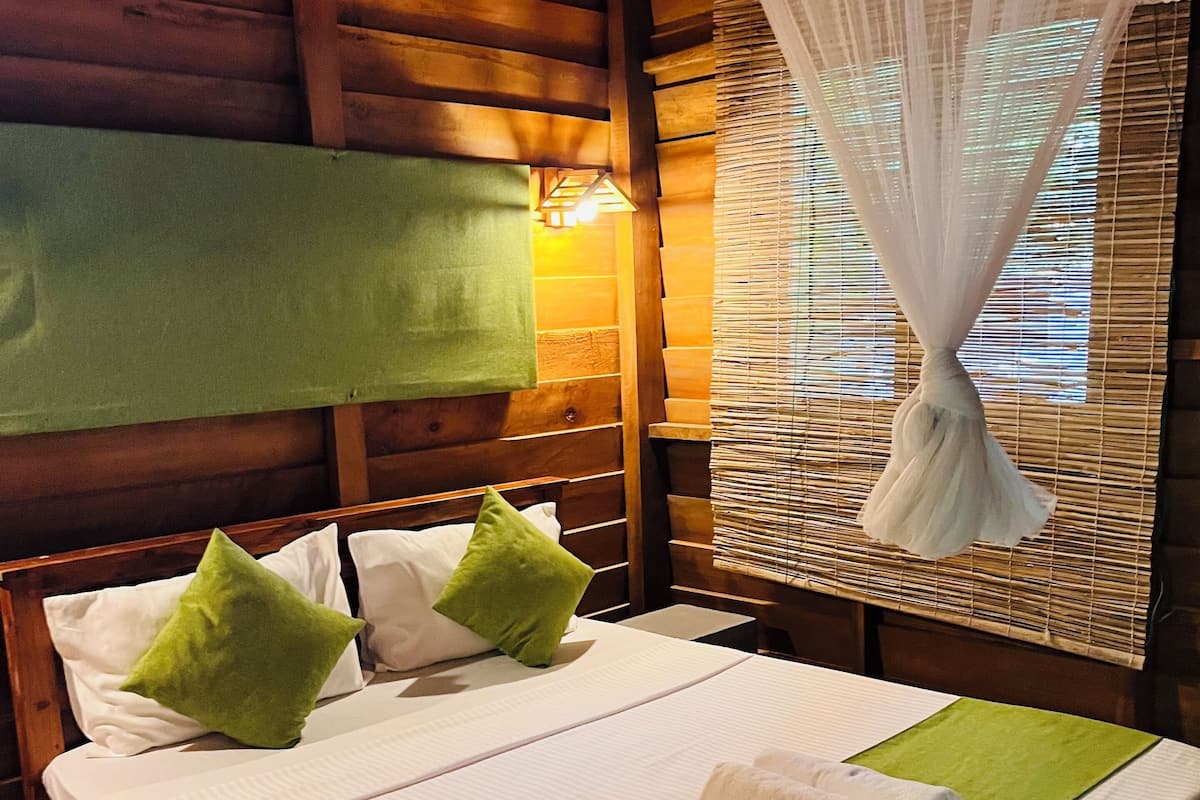A wooden bed with a green and white bedspread, two pillows, and a rolled towel.
