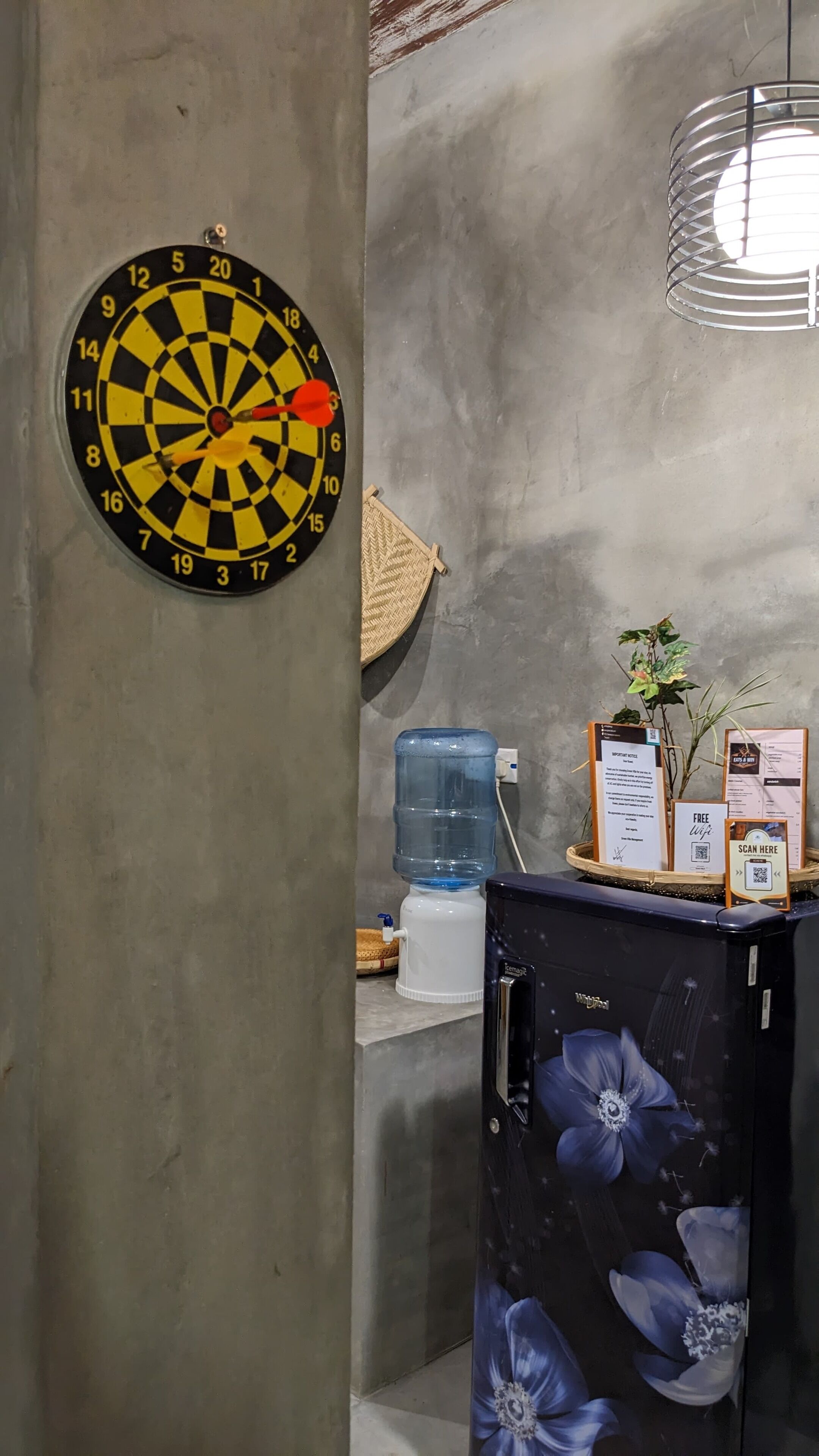 Un tablero de dardos, un dispensador de agua, un tablero de menú y un mueble con estampado floral.