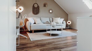 A modern loft bedroom with a sloped ceiling, a light blue sofa, a glass coffee table, and a white desk with a lamp. - Wohnungtraveller Geislautern (Völklingen)