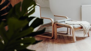 A modern lounge chair with a wooden frame and a light-colored cushion, positioned next to a white radiator. - Wohnungtraveller Geislautern (Völklingen)