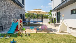 Un jardin avec un trampoline, un espace de jeux et un tipi.