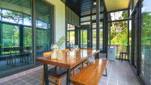 A modern dining area with a long wooden table, benches, and a view of the outdoors through large windows.