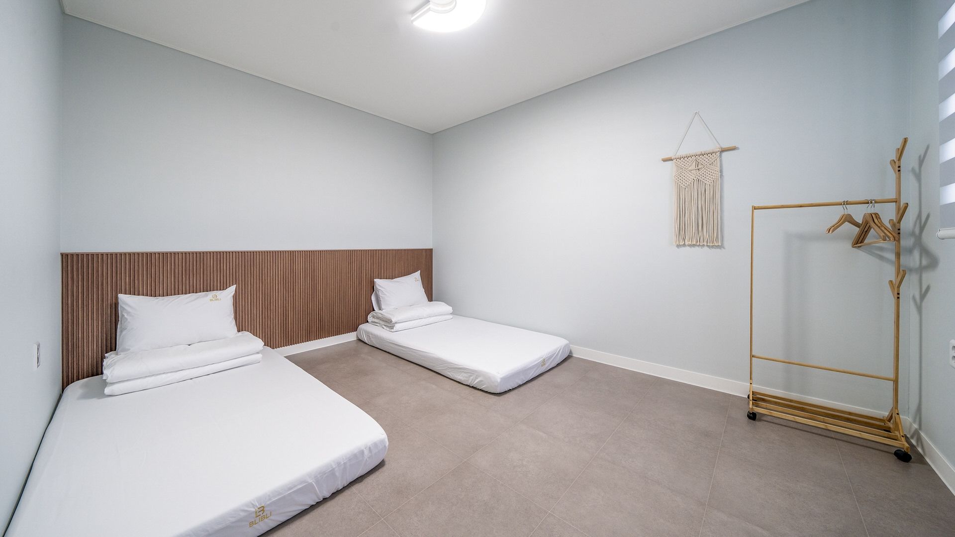 Een hotelkamer met twee eenpersoonsbedden, een houten hoofdbord, een macramé wanddecoratie en een houten kapstok.