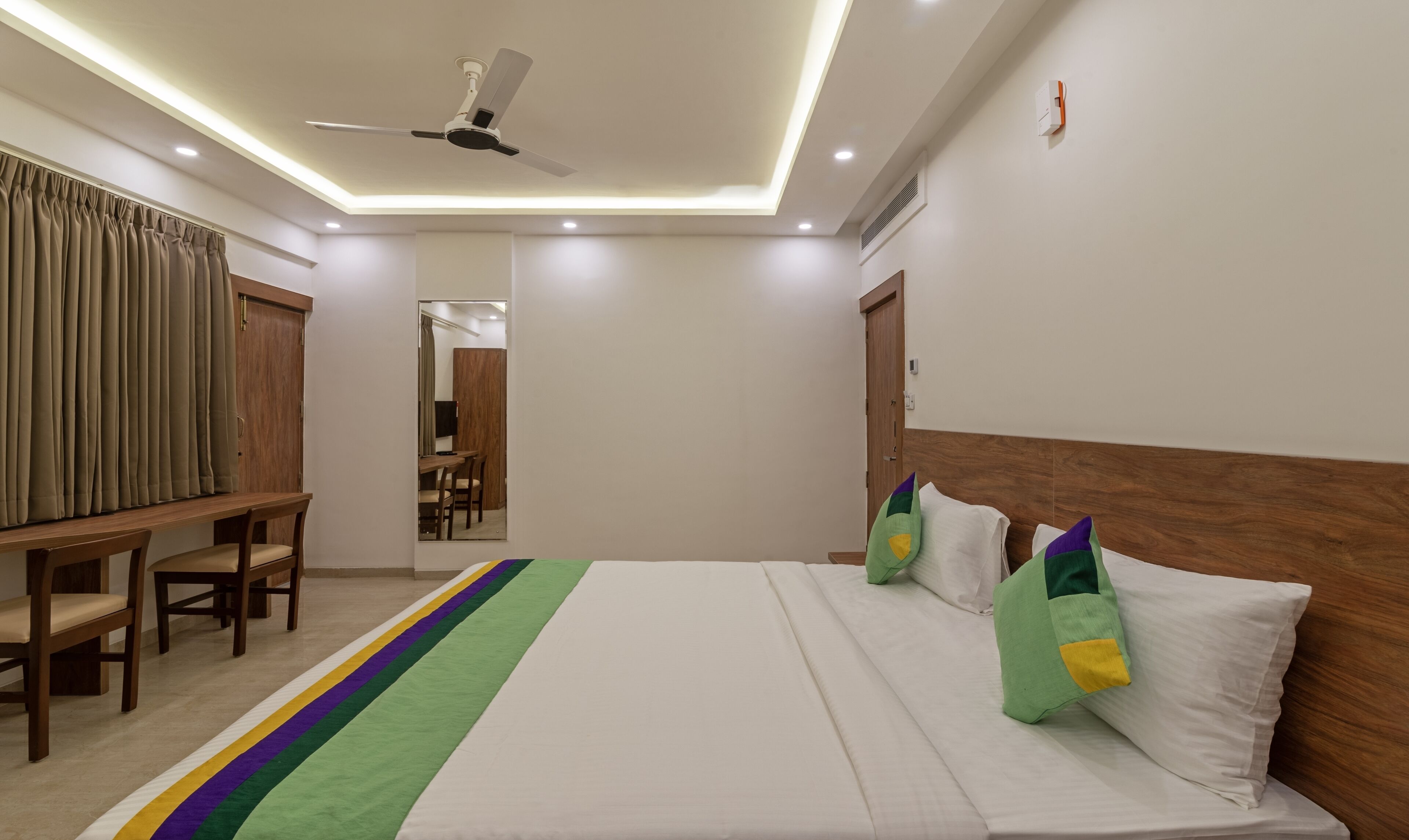 A hotel room with a bed, a ceiling fan, a desk, and a chair.