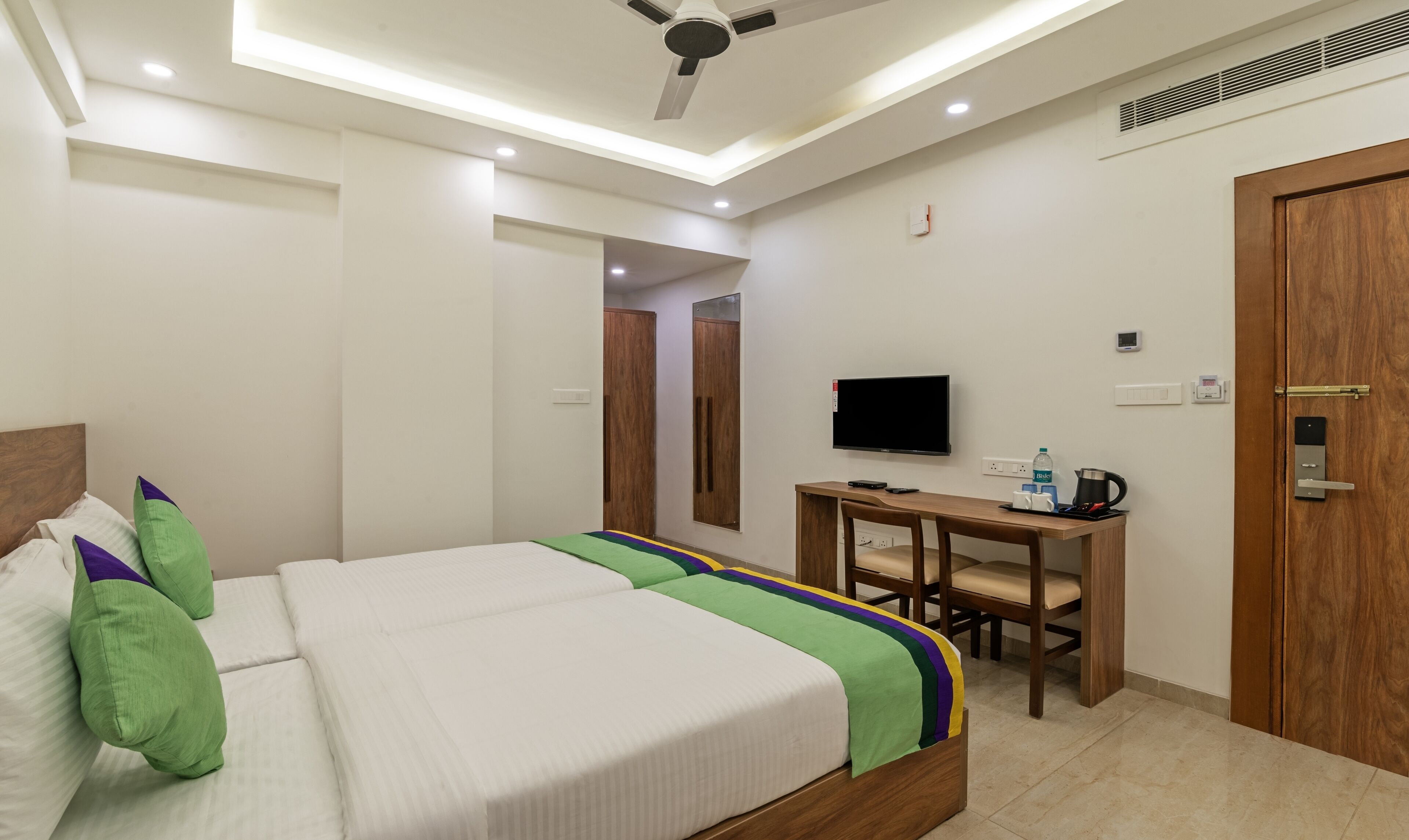 A hotel room with a bed, a desk, a television, and a door.