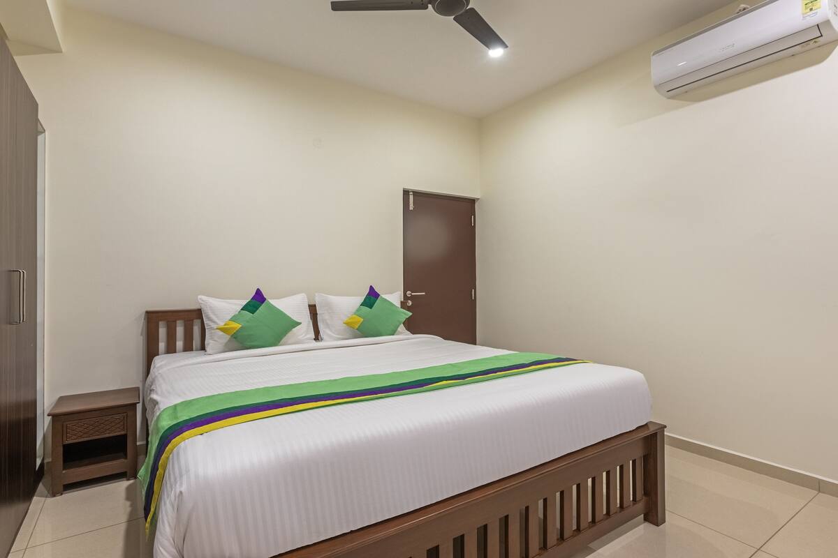 Ein Schlafzimmer mit einem Bett, einem Holzschrank, einem Nachttisch, einem Deckenventilator und einer Klimaanlage.