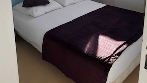Quarto com cama, mesa de cabeceira, luminária e janela com vista para edifícios.