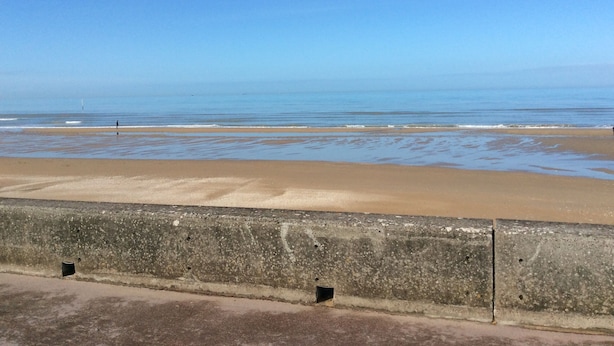 Uma praia com uma barreira de concreto ao primeiro plano.