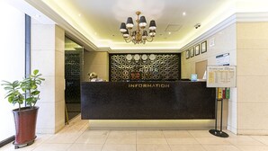 Un mostrador de recepción de hotel con encimera de mármol negro, una araña colgante y una pared decorativa con patrones geométricos.