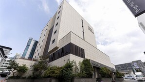 Un hotel moderno con una imponente torre en esquina, un área exterior bien cuidada con jardineras y un cielo despejado.