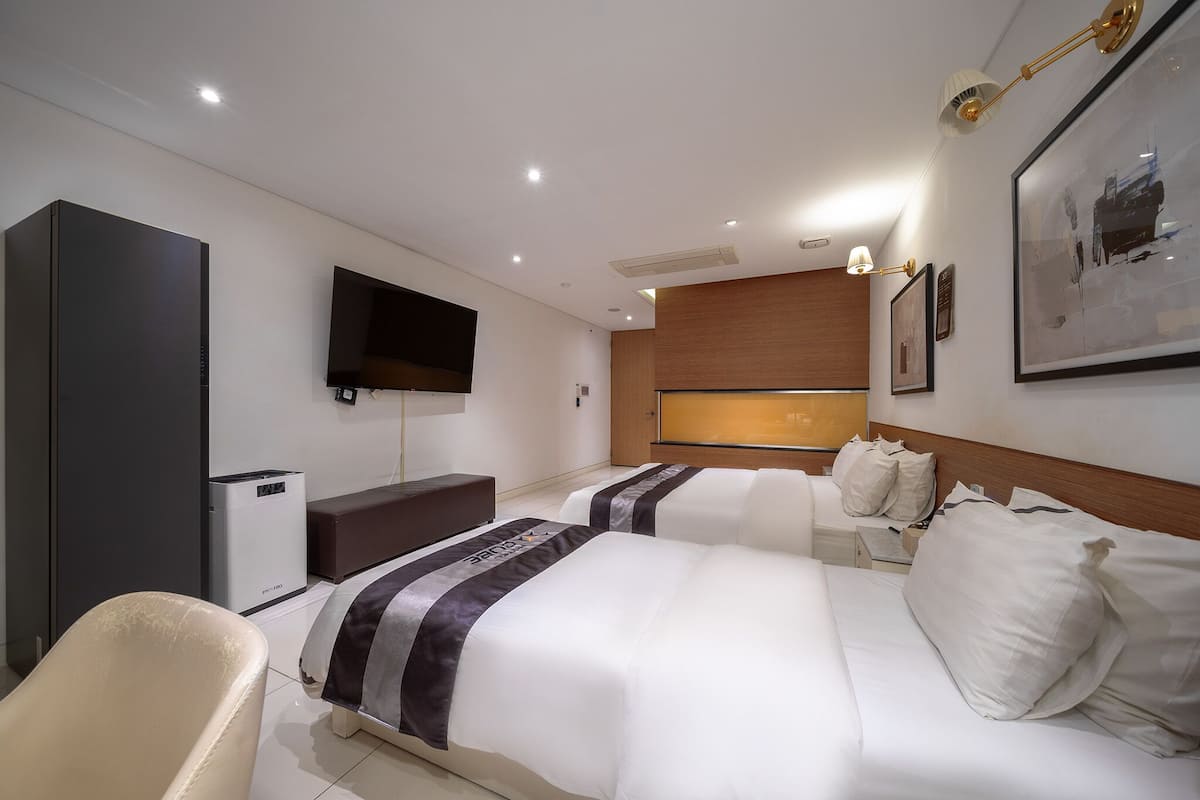 A hotel room with two beds, a TV, a desk, and a large window.