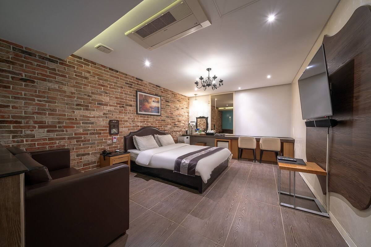 A modern bedroom with a brick wall, a bed, a desk, and a TV.