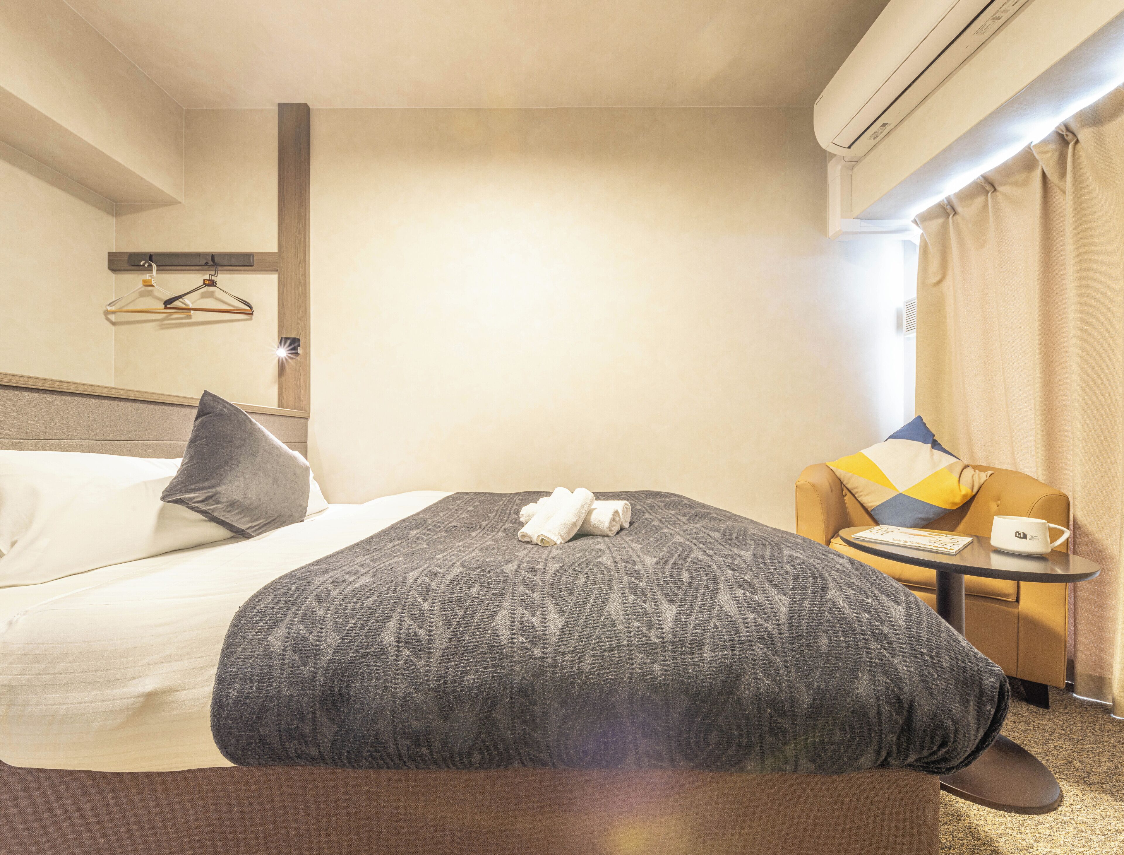 Et hotelværelse med en seng, en stol, et lille bord og en aircondition.