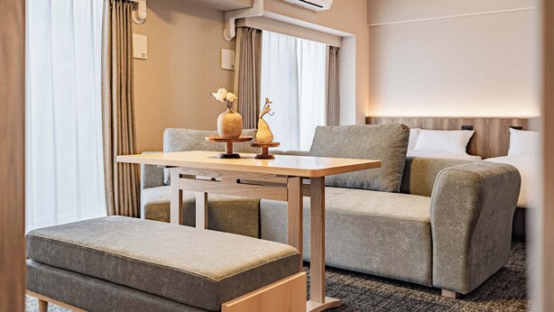 Ein modernes Hotelzimmer mit Sofa, Hocker und einem kleinen Tisch mit Dekoration.