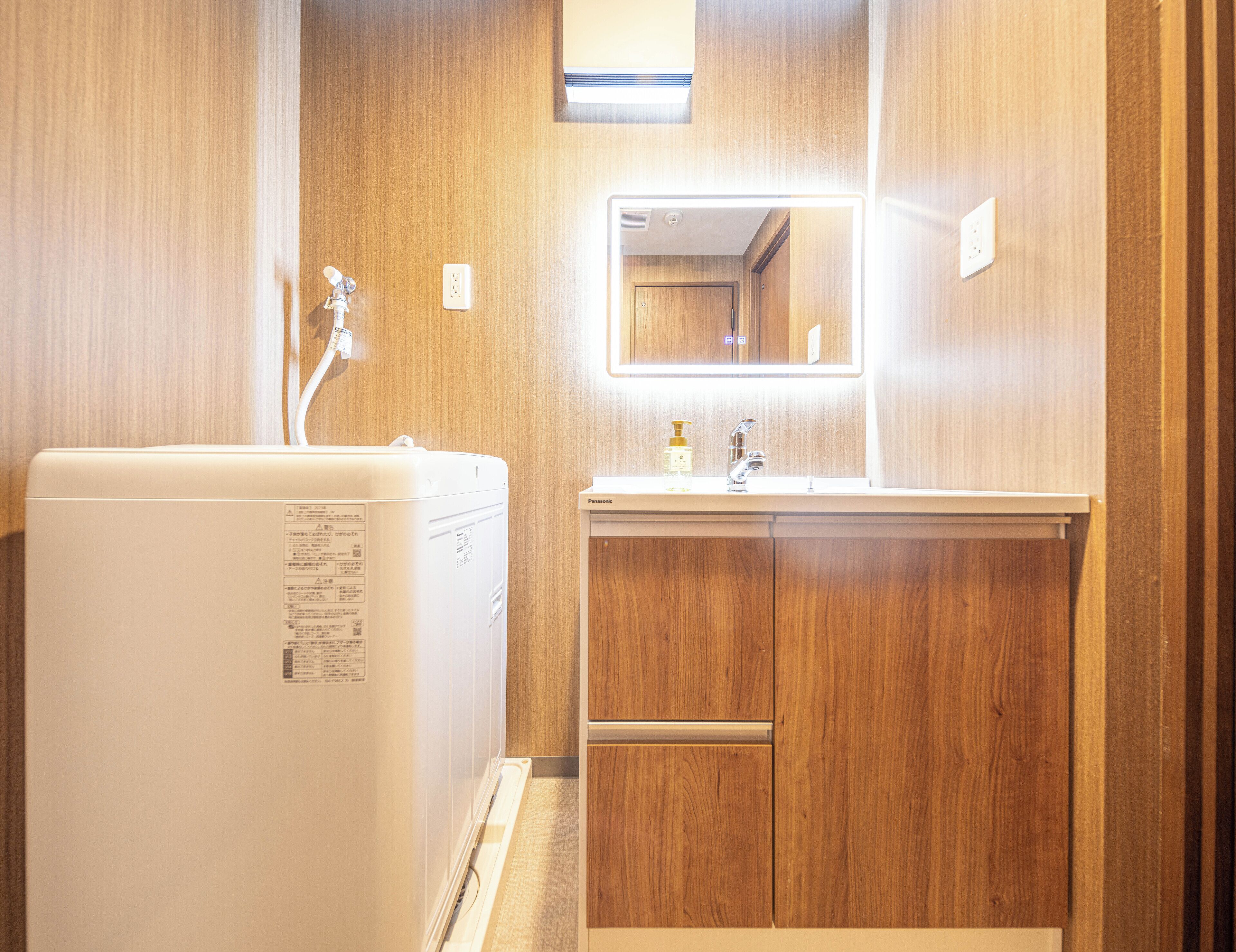Ett litet badrum med träpanel på väggarna, ett vitt handfat med en spegel ovanför och en vit apparat, troligen en tvättmaskin eller torktumlare, till vänster.