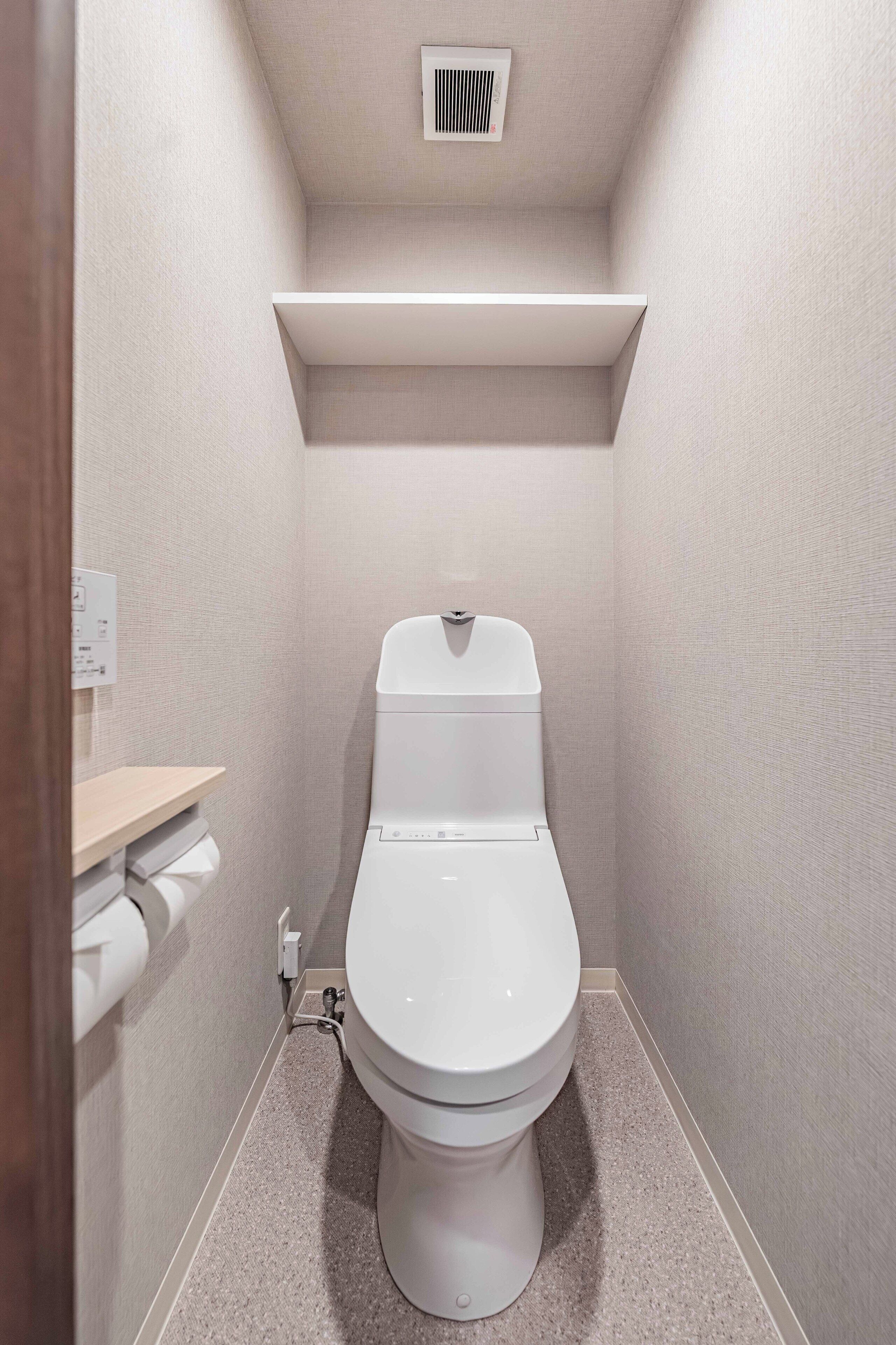 Casa de banho compacta com sanita, prateleira na parede e ventilação no teto.