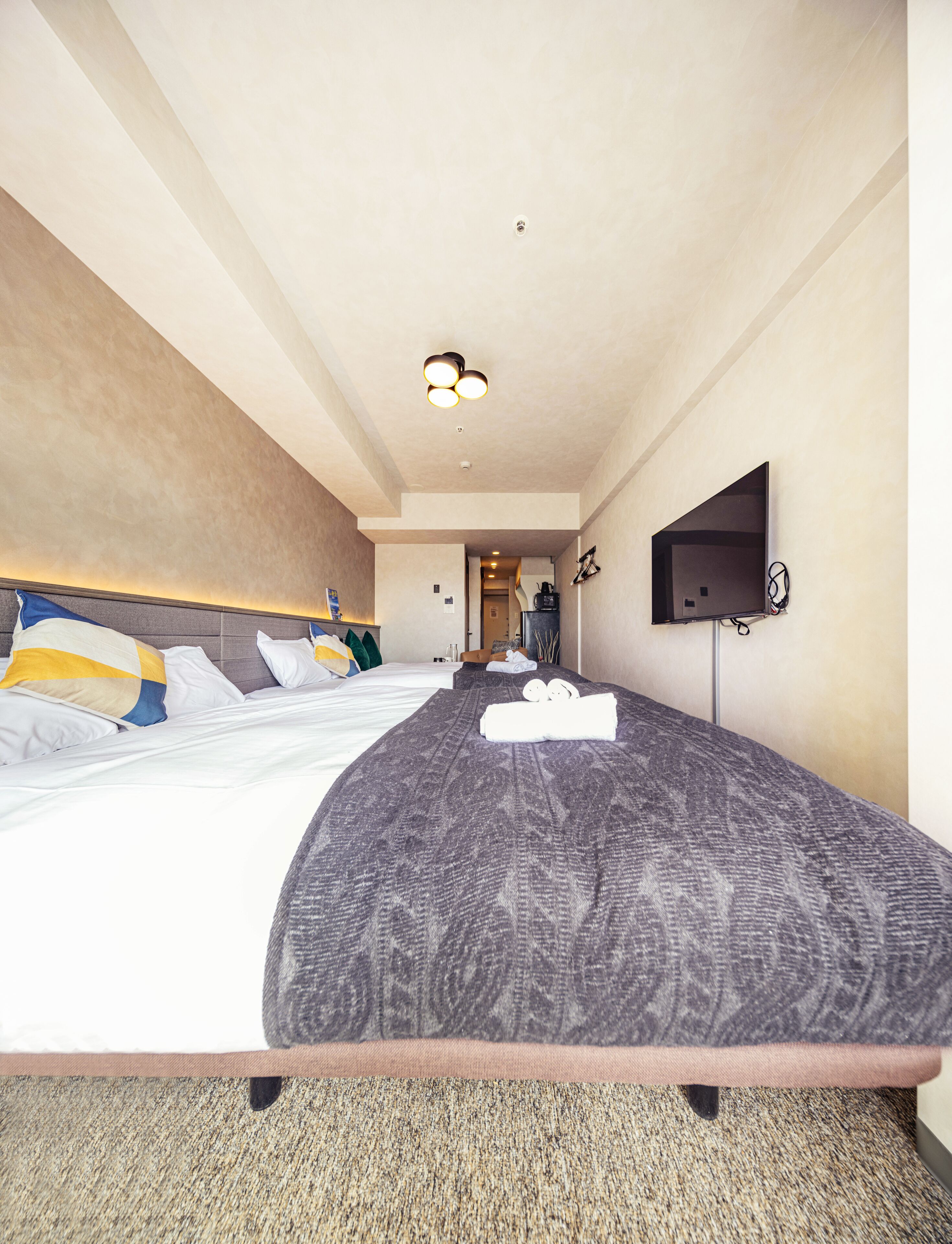 A hotel room with a large bed, a flat-screen TV mounted on the wall, and a ceiling light fixture.