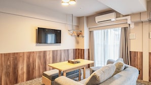 A modern hotel room with a sofa, a small table, a flat-screen TV, and an air conditioning unit. - Apartment Hotel 11 Shinsaibashi II (Osaka)