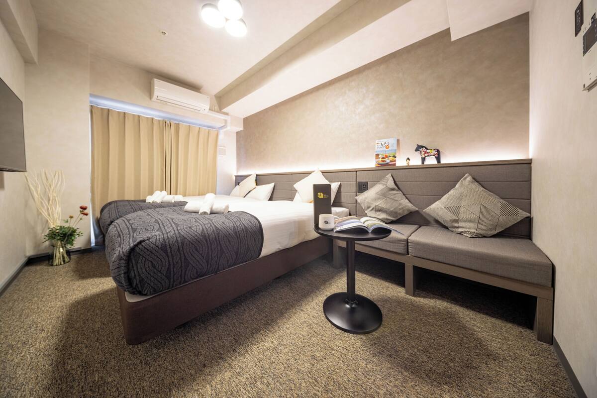 Une chambre d’hôtel moderne, équipée d’un lit, d’un canapé, d’une table basse et d’une petite table sur laquelle se trouvent un livre et une tasse.