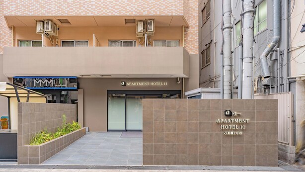 A modern building with a sign for 'Apartment Hotel 11' and a gated entrance. - Apartment Hotel 11 Shinsaibashi II (Osaka)