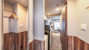 Ein Hotelkorridor mit Holzwandverkleidung, einem Kleiderständer, einem Kühlschrank und einer Küchenzeile.