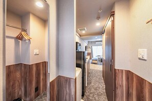 Un couloir d’hôtel avec des boiseries, un porte-manteau, un réfrigérateur et un coin cuisine.