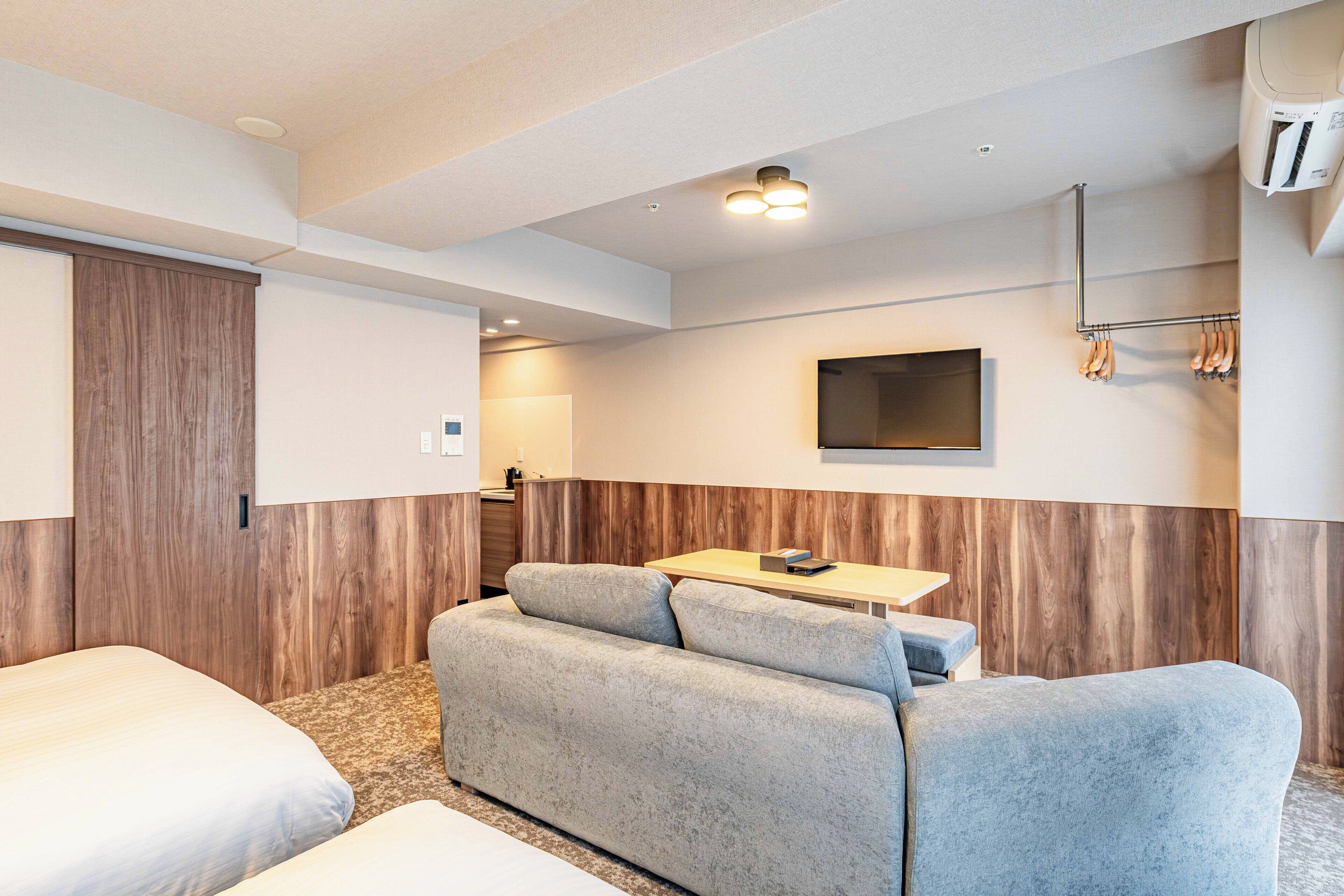 A hotel room with a sofa, a bed, a TV, and a coat rack.