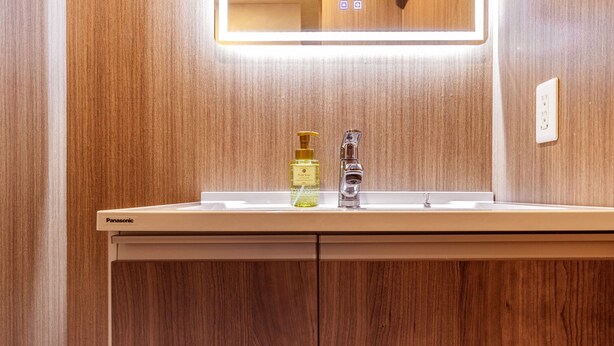 Une salle de bain avec un meuble-lavabo en bois, un miroir avec éclairage intégré et un lavabo.