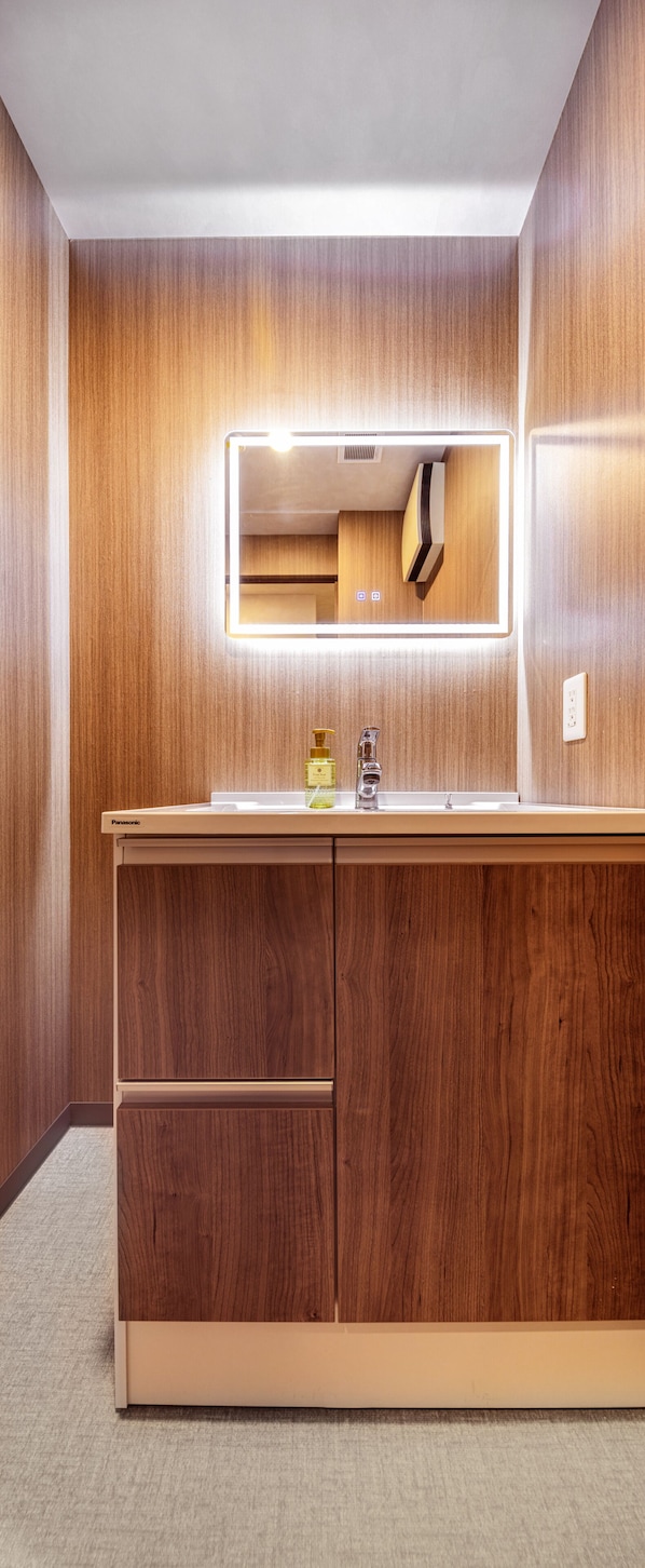 Ein Badezimmer mit einem Holzkosmetikschrank, einem beleuchteten Spiegel und einem Waschbecken.