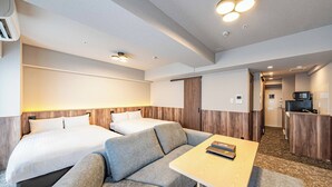 Ein Hotelzimmer mit zwei Betten, einem Schlafsofa, einem kleinen Tisch und einer Küchenzeile.