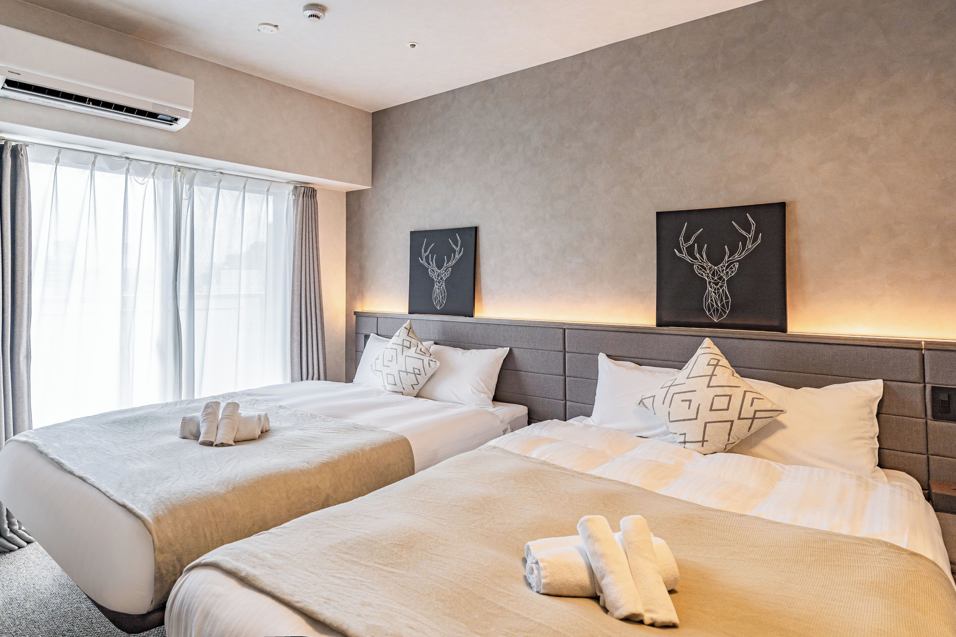 A hotel room with two beds, a large window with curtains, and artwork on the wall.