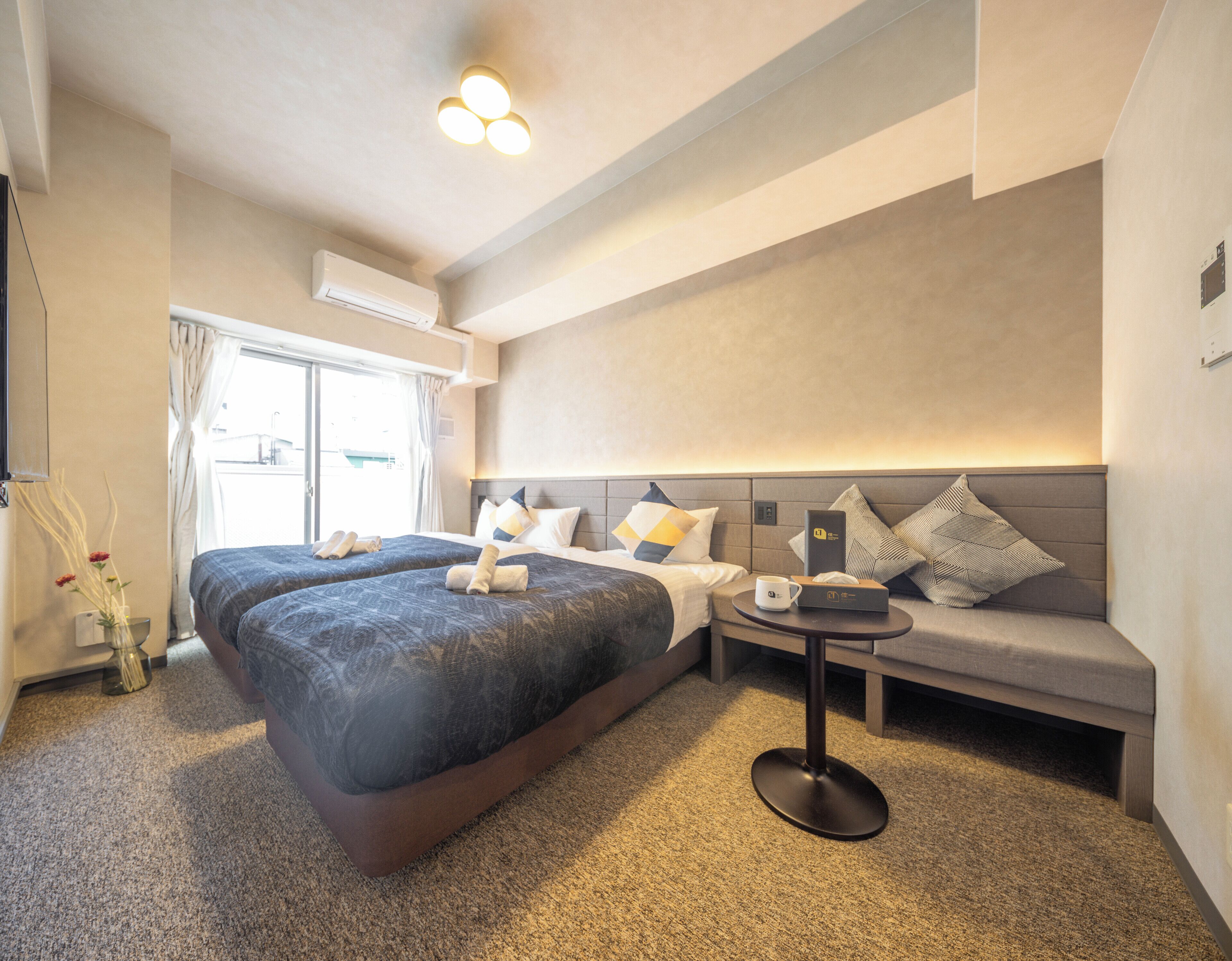 Ein Hotelzimmer mit zwei Betten, einem Schlafsofa, einem kleinen Tisch und einem Fenster mit Vorhängen.