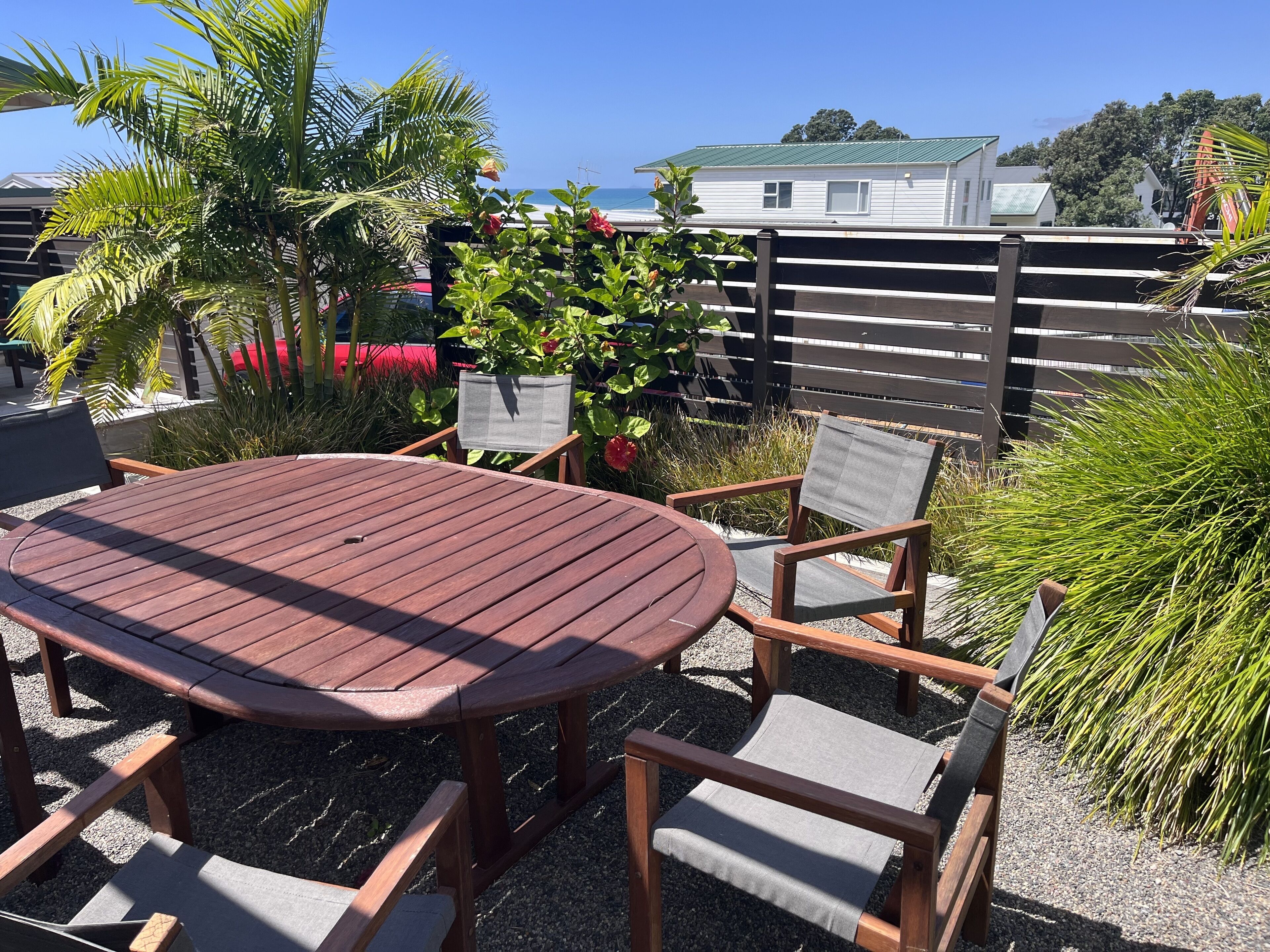 A wooden table and chairs set outdoors with a view of a house and trees in the background.