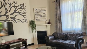 A living room with a black leather sofa, a glass coffee table, a TV on a stand, a fireplace, and a decorative wall piece.