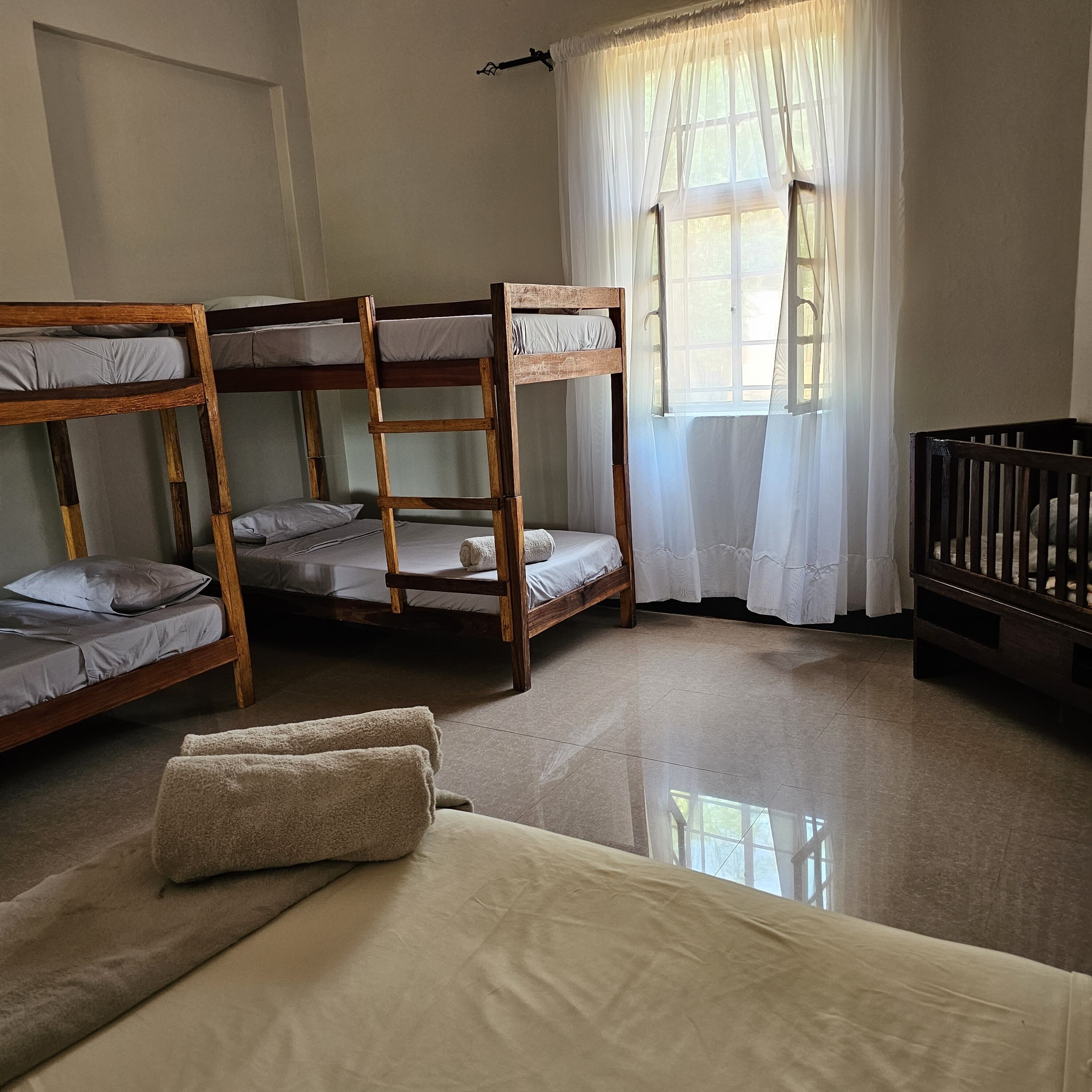 Une chambre de dortoir avec des lits superposés, un berceau et une grande fenêtre avec des rideaux.