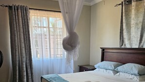Uma cama bem arrumada com duas toalhas enroladas, uma mesa de cabeceira e um criado-mudo.