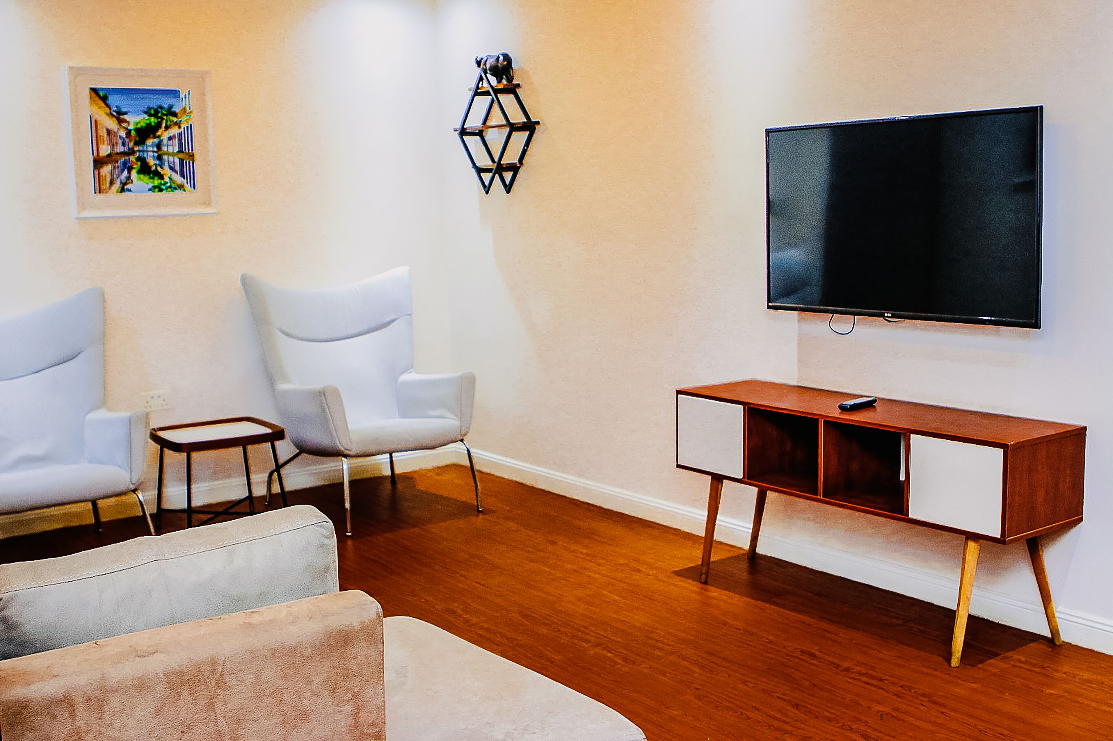 Una sala de estar con televisor, sillas blancas, un mueble de madera y una mesita.