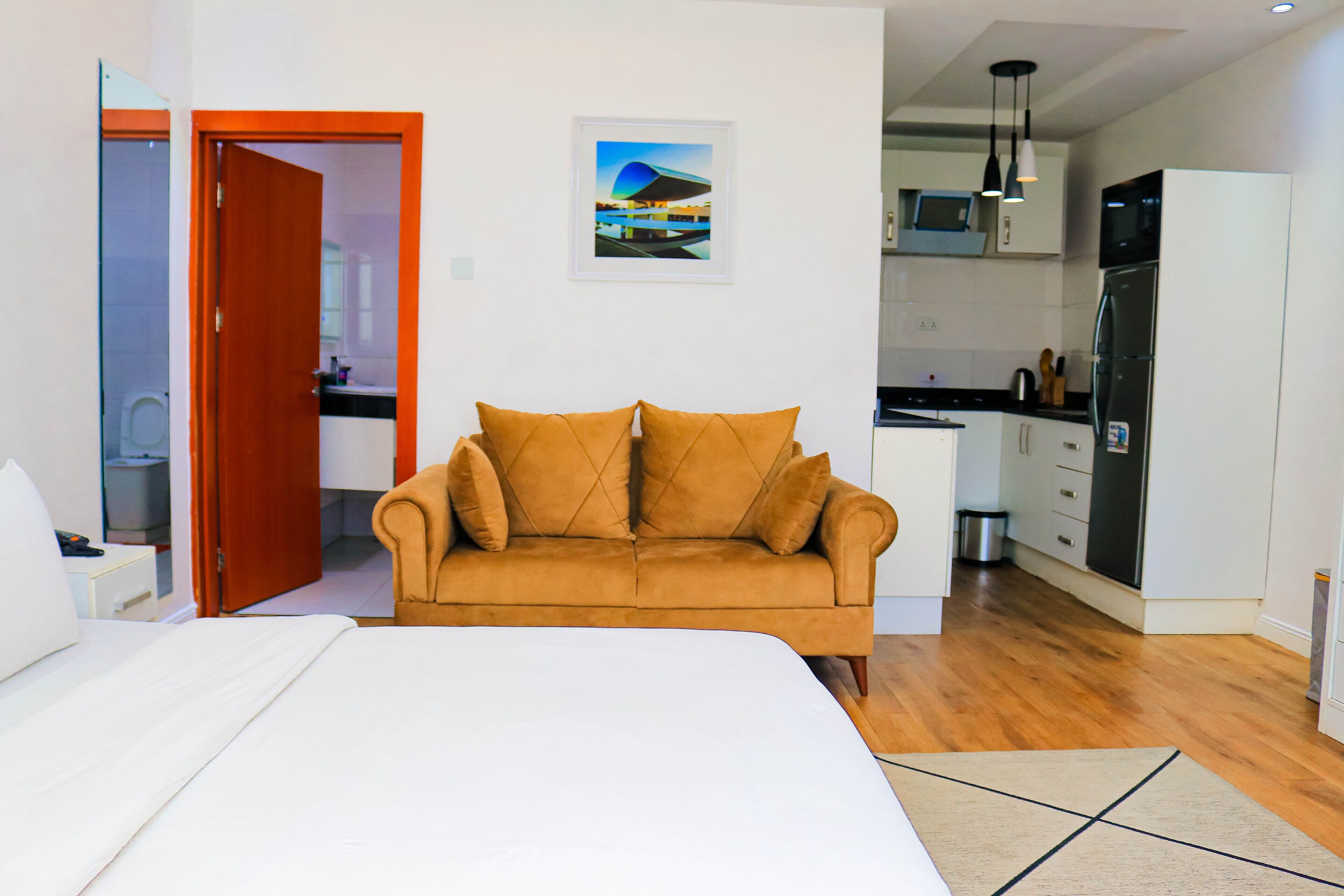 A bedroom with a bed, a sofa, and a kitchen area with a refrigerator and microwave.