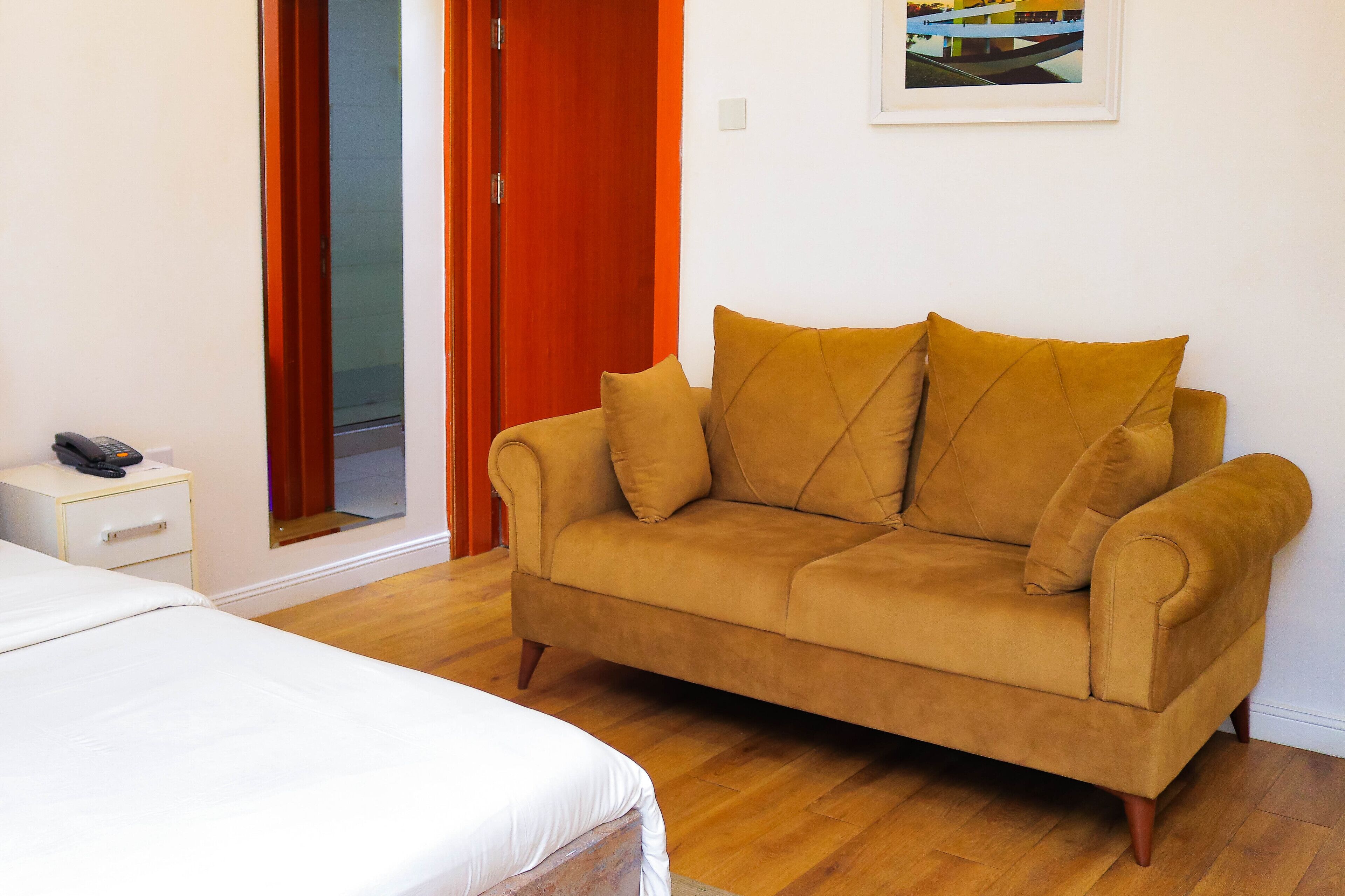 A room with a beige sofa, a white bedside table, and a wooden floor.