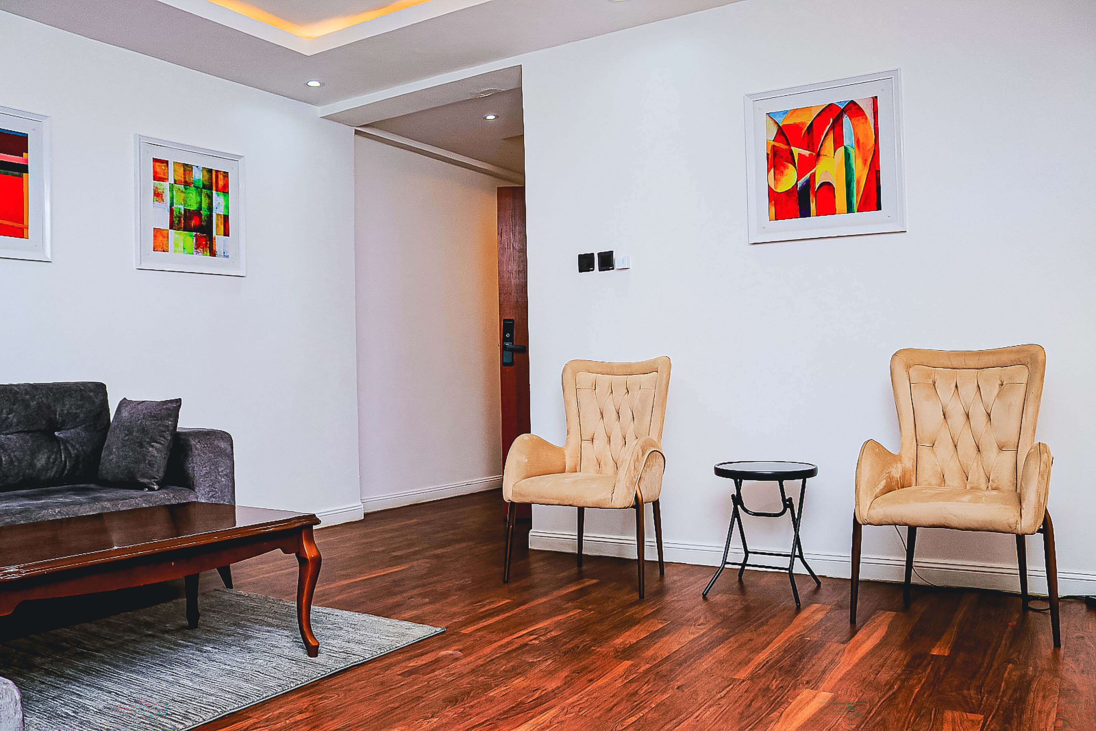 Ein modernes Wohnzimmer mit Holzboden, einem grauen Sofa, zwei Sesseln, einem Couchtisch und Bildern an den Wänden.
