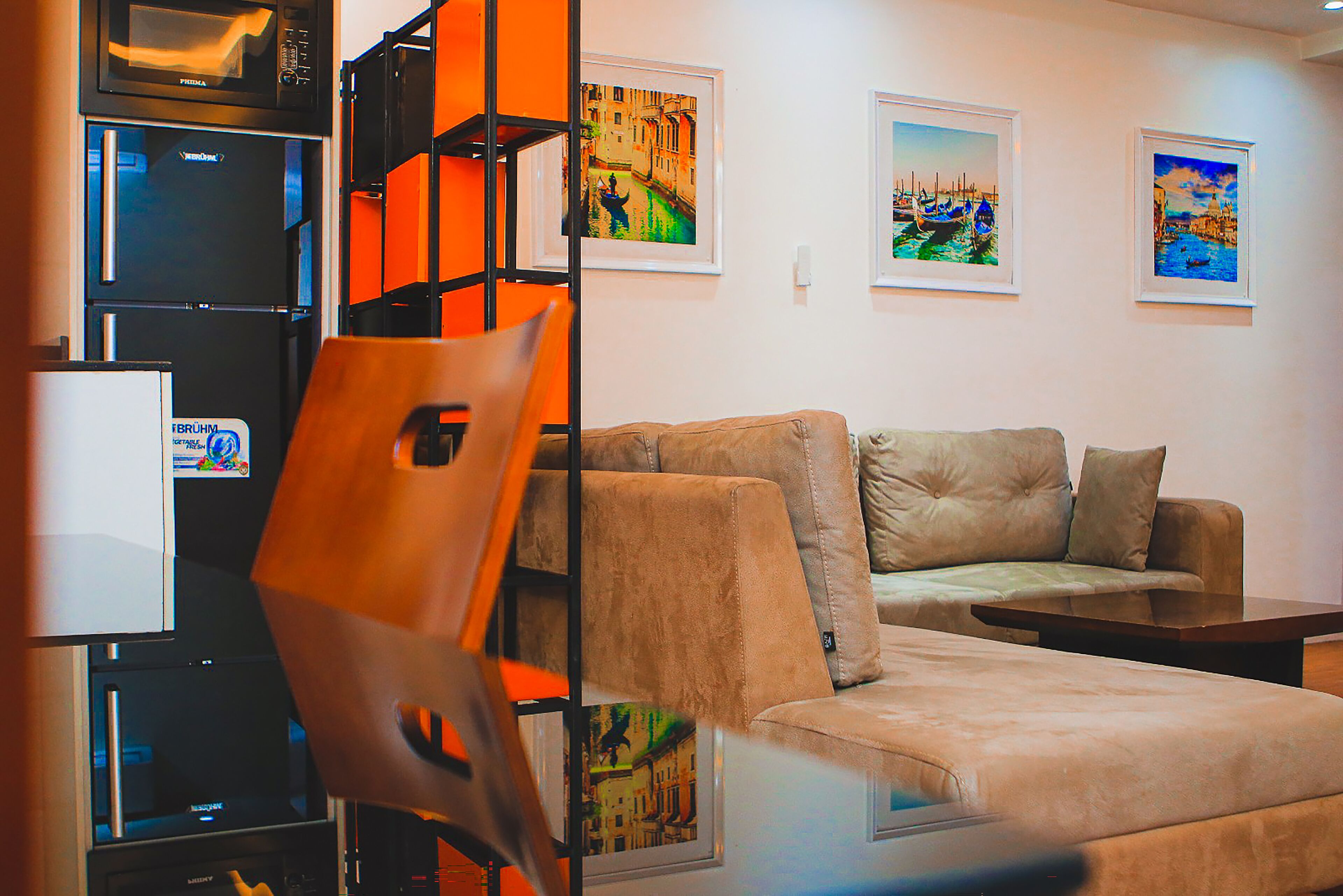 A modern living room with a sofa, a coffee table, and a TV. There are framed pictures on the wall and a black shelving unit.