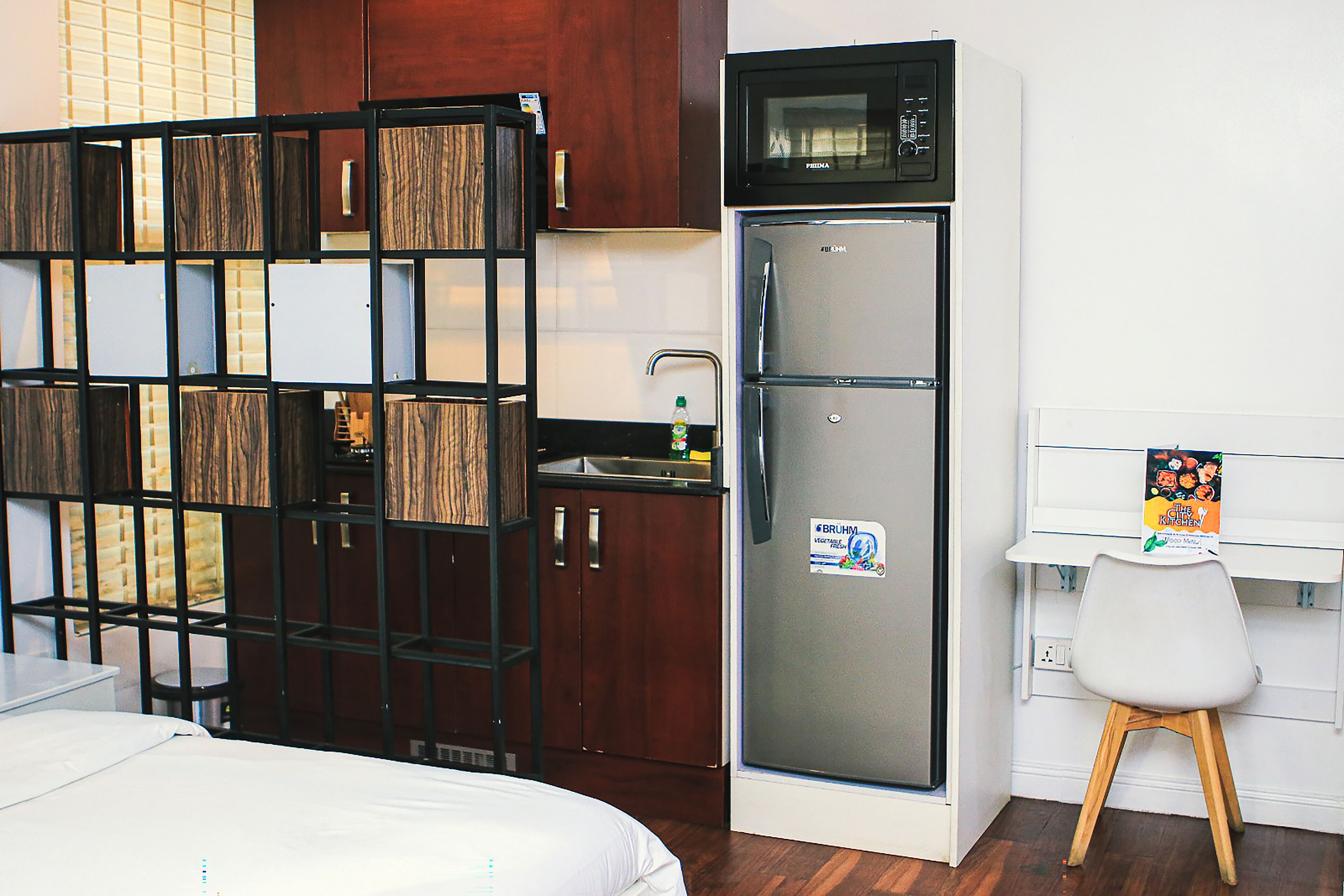 Camera d'albergo compatta con un letto, angolo cottura, frigorifero e una piccola scrivania con sedia.