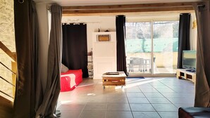 Una habitación con un sofá rojo, una mesa de centro de madera, un televisor sobre un mueble de madera y un amplio ventanal corredero que da a un área exterior.