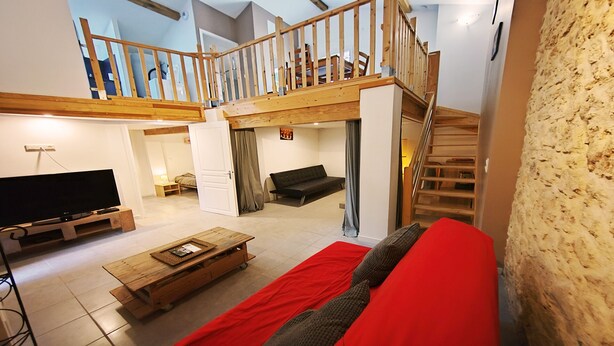 Un amplio salón con una escalera de madera, un televisor de pantalla plana, un sofá rojo y una mesa de centro.