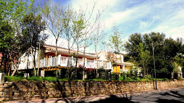 A two-story building with a balcony, surrounded by trees and a stone wall. - Résidence Le Manaka, Le Mazet (Lamalou-les-Bains)