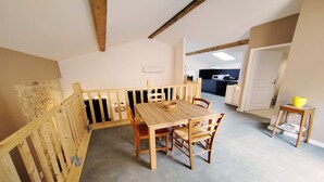 Un comedor con una mesa y sillas de madera, una mesita auxiliar con un tazón amarillo, y una cocina al fondo.